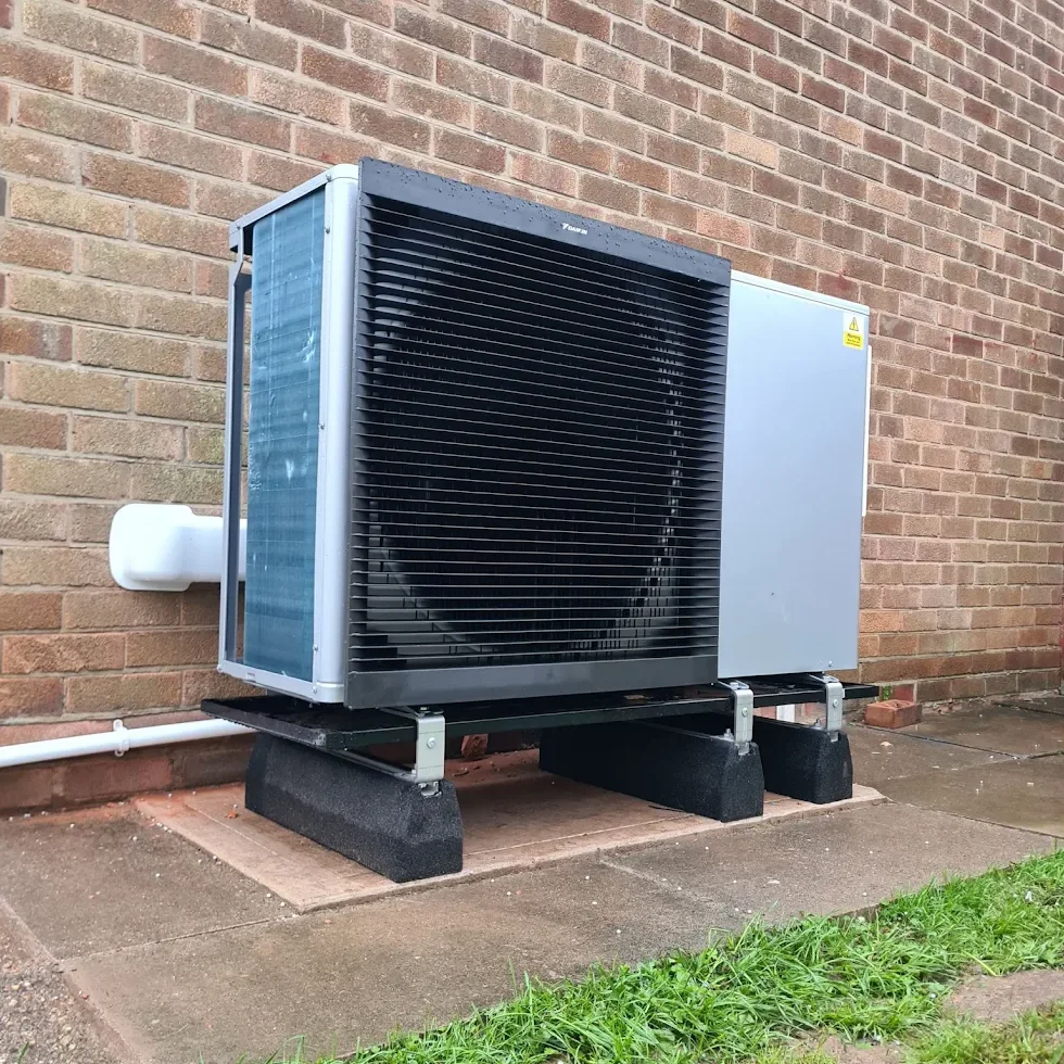 Air source heat pump outdoor unit installed against a brick wall