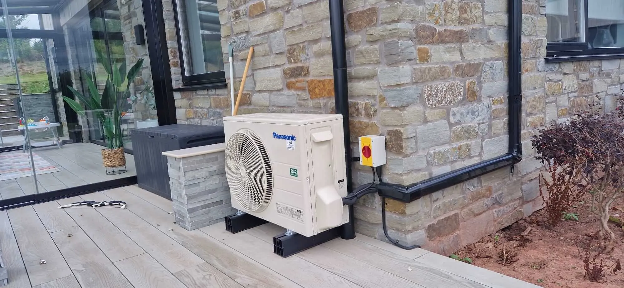 Panasonic air conditioning outdoor unit on anti-vibration feet beside a stone wall