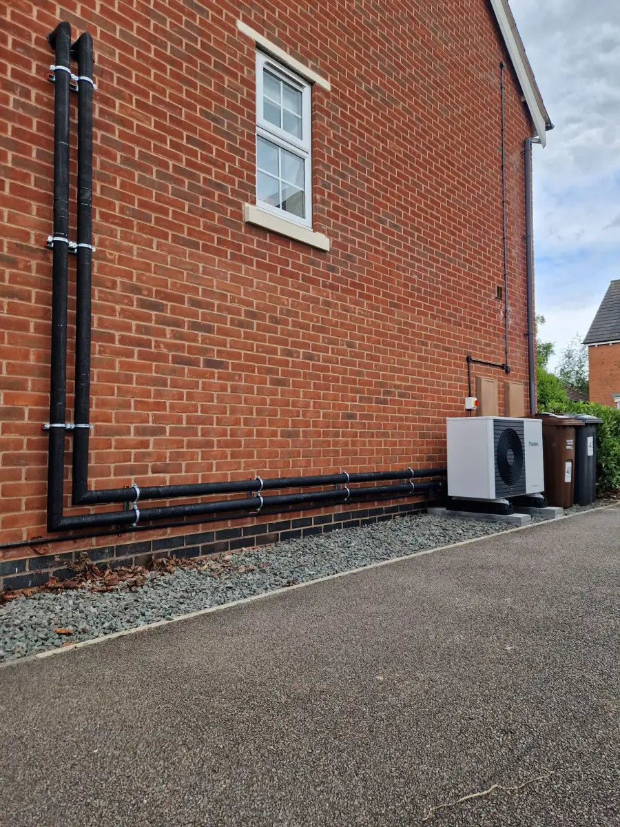 External insulated pipework run along a brick wall to an outdoor heat pump unit